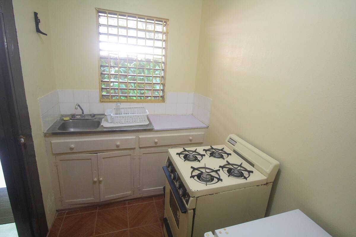 A small kitchen with a gas stove, a sink, and a window with bars.