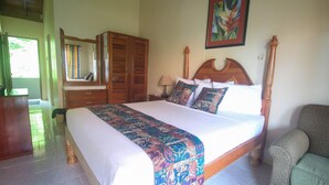 A bedroom with a large bed, wooden wardrobe, and a chair. - Moon Rooms at Moonrise Villa (Negril)