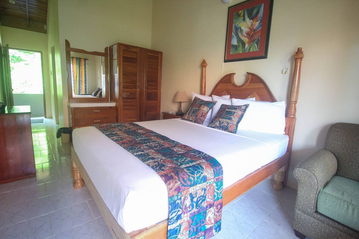 A bedroom with a large bed, wooden wardrobe, and a chair.