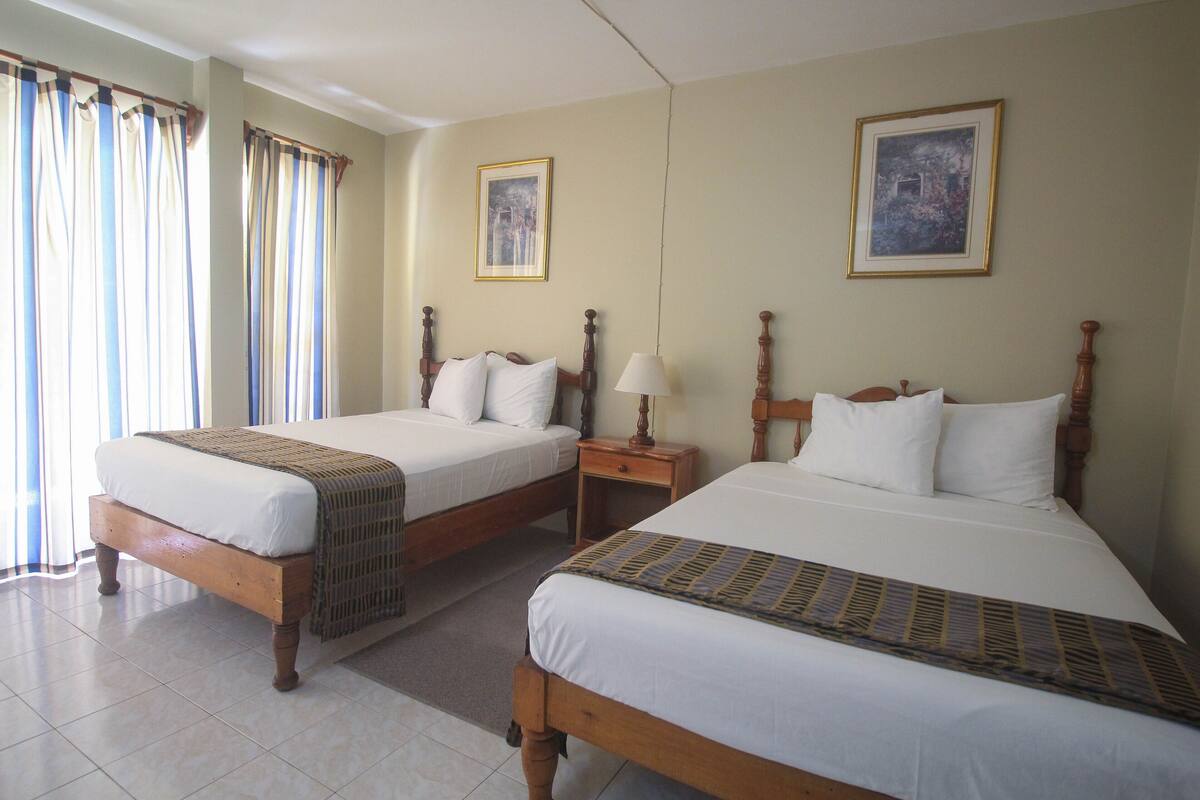 A hotel room with two wooden beds, a nightstand, a lamp, and two framed pictures on the walls.