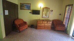A room with two patterned armchairs, a wooden dresser, a television, and a mirror on the wall. - Moon Rooms at Moonrise Villa (Negril)