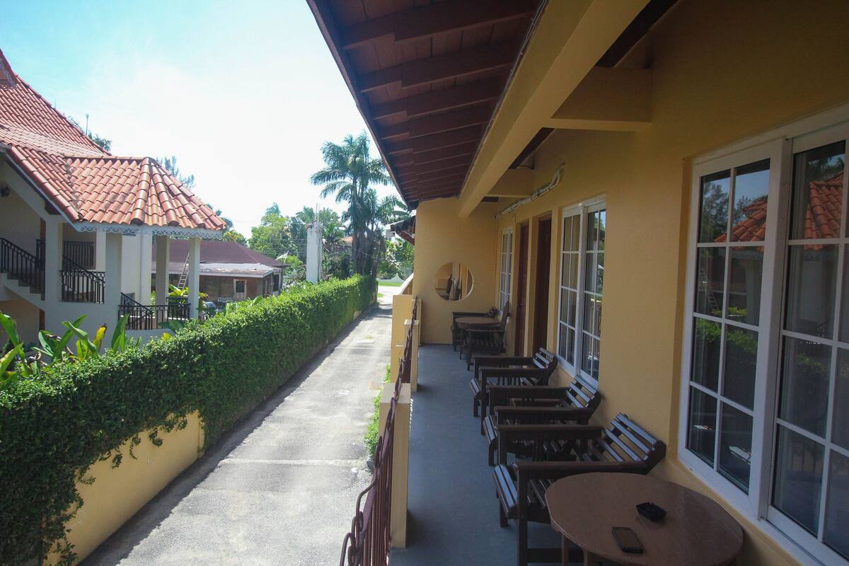 A building with a covered outdoor seating area, a paved walkway, and a row of windows.