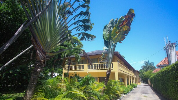 A yellow building with a balcony, surrounded by lush tropical vegetation. - Moon Rooms at Moonrise Villa (Negril)