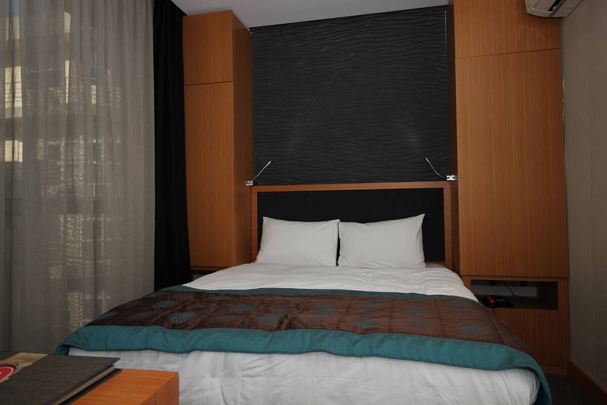 A neatly made bed with white and teal bedding, a wooden headboard, and a black accent wall.