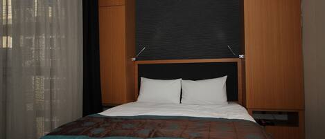 Una cama bien hecha con ropa de cama blanca y azul verdoso, un cabecero de madera y una pared de acento negra.