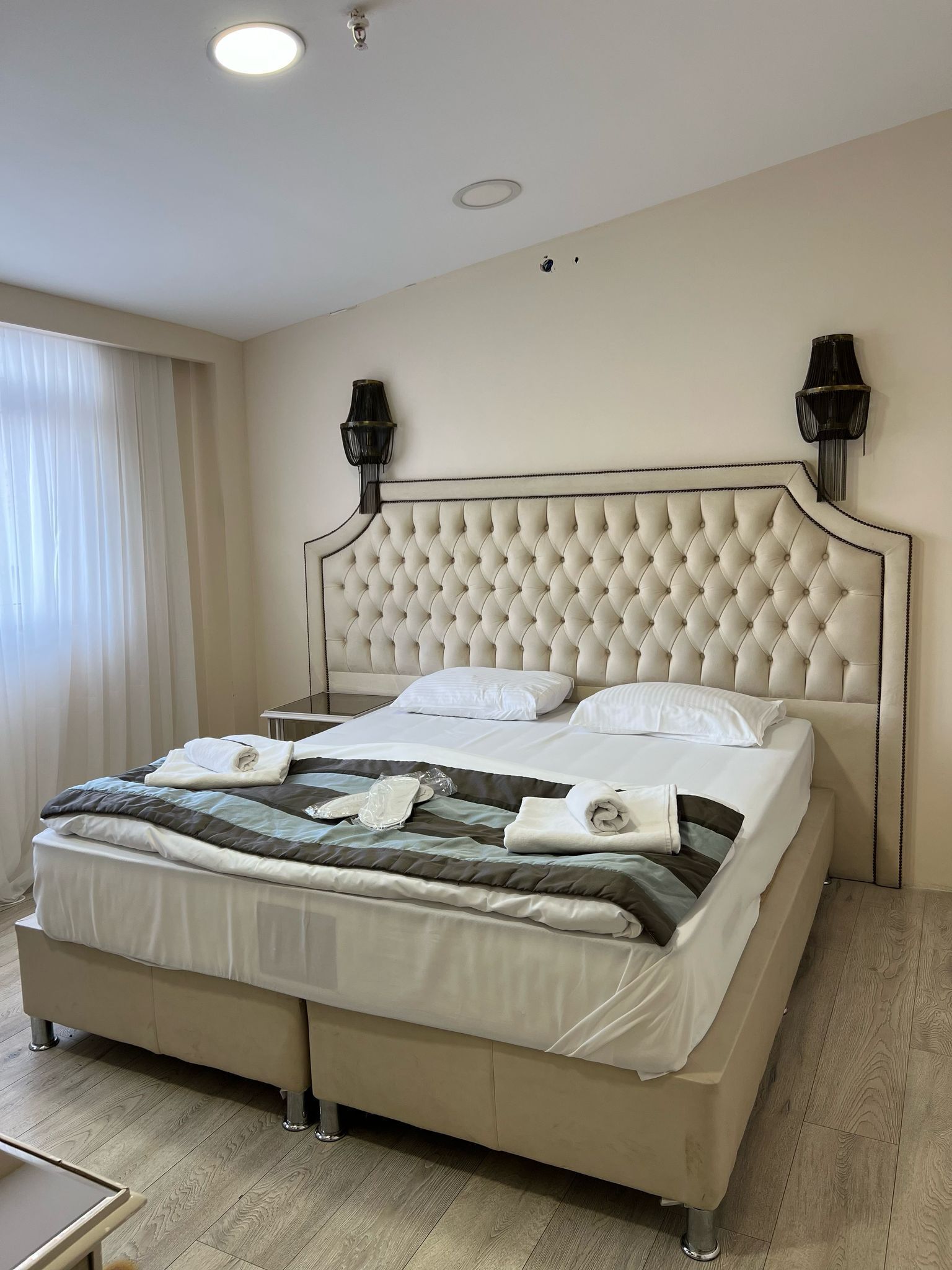 A neatly made bed with white linens and a quilt, a tufted headboard, and two wall-mounted lamps.