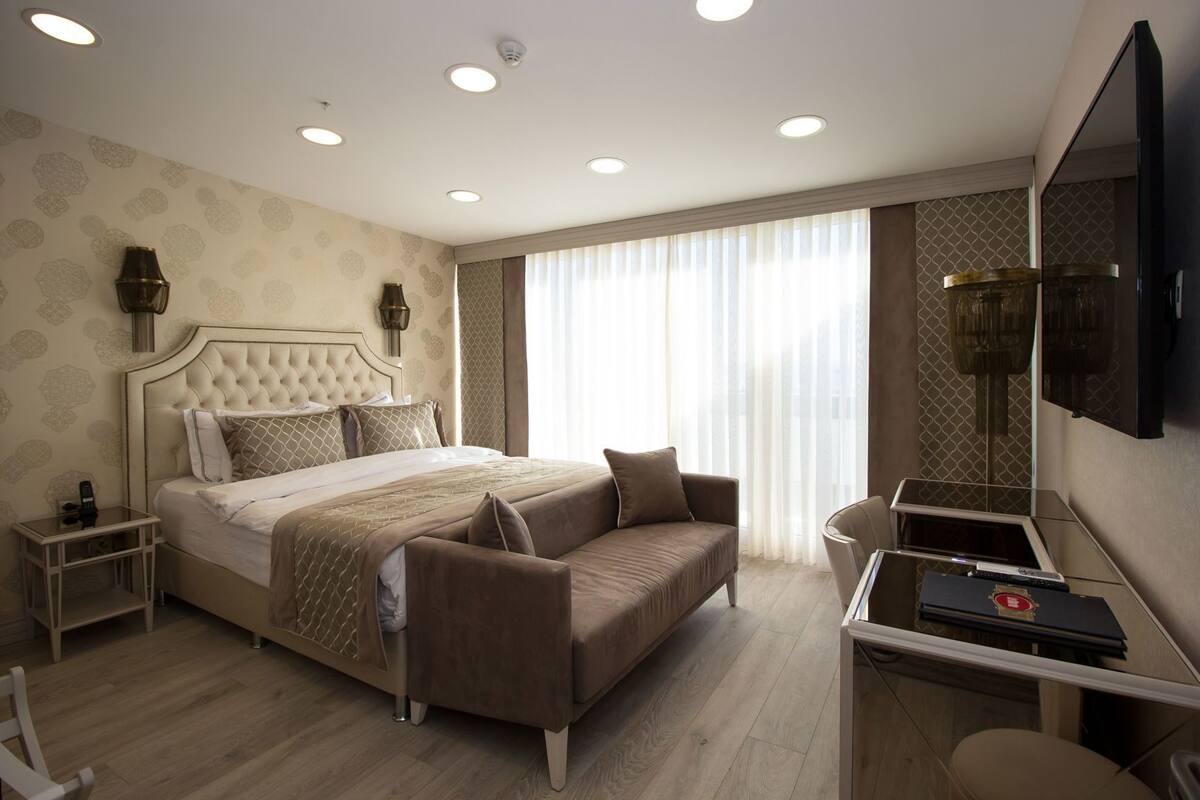 A modern hotel room with a large bed, a sofa, a desk, and a flat-screen TV.