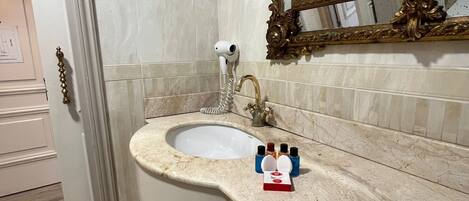 A bathroom with a marble sink, a gold-framed mirror, and a wall-mounted light fixture.