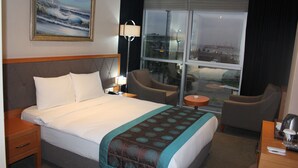 A hotel room with a large bed, a desk, two armchairs, a window with a city view, and a painting on the wall. - Le Marde Hotel (Istanbul)