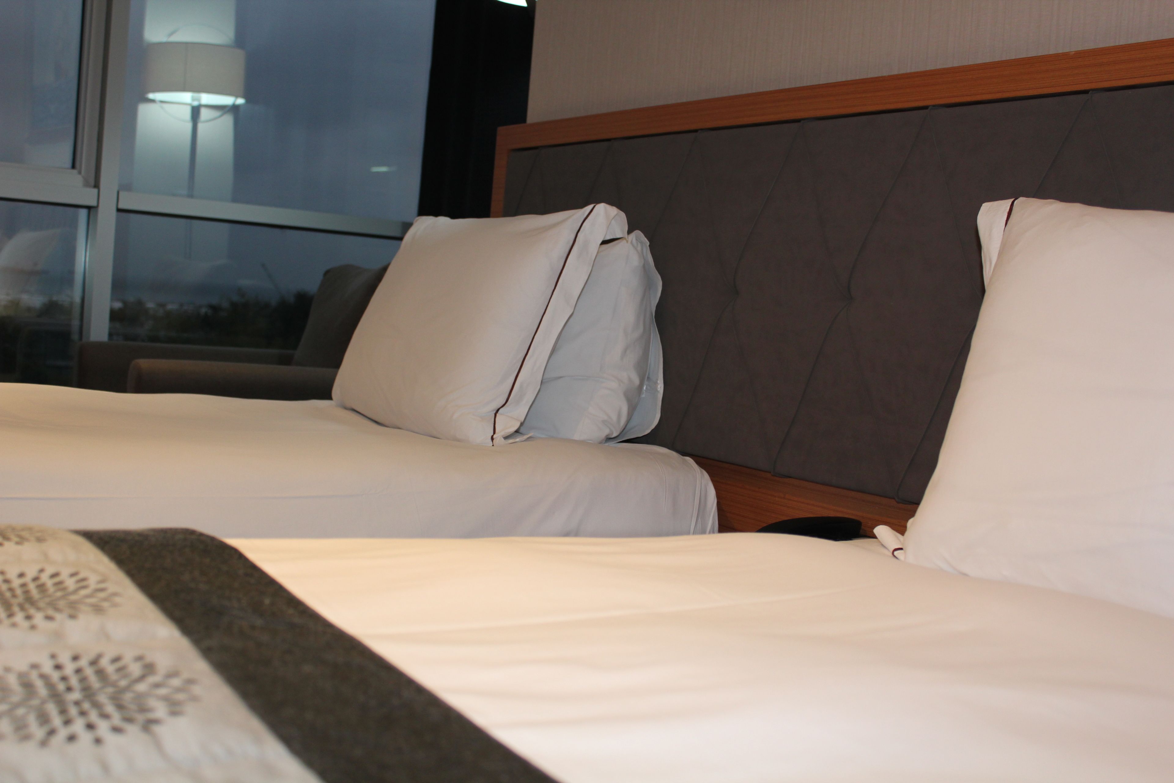 Habitación de hotel con dos camas, un ventanal grande y un cabecero moderno.