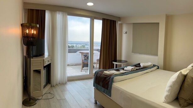 A hotel room with a bed, a desk with a lamp, a small table, and a view of the outdoors through a sliding door. - Le Marde Hotel (Istanbul)