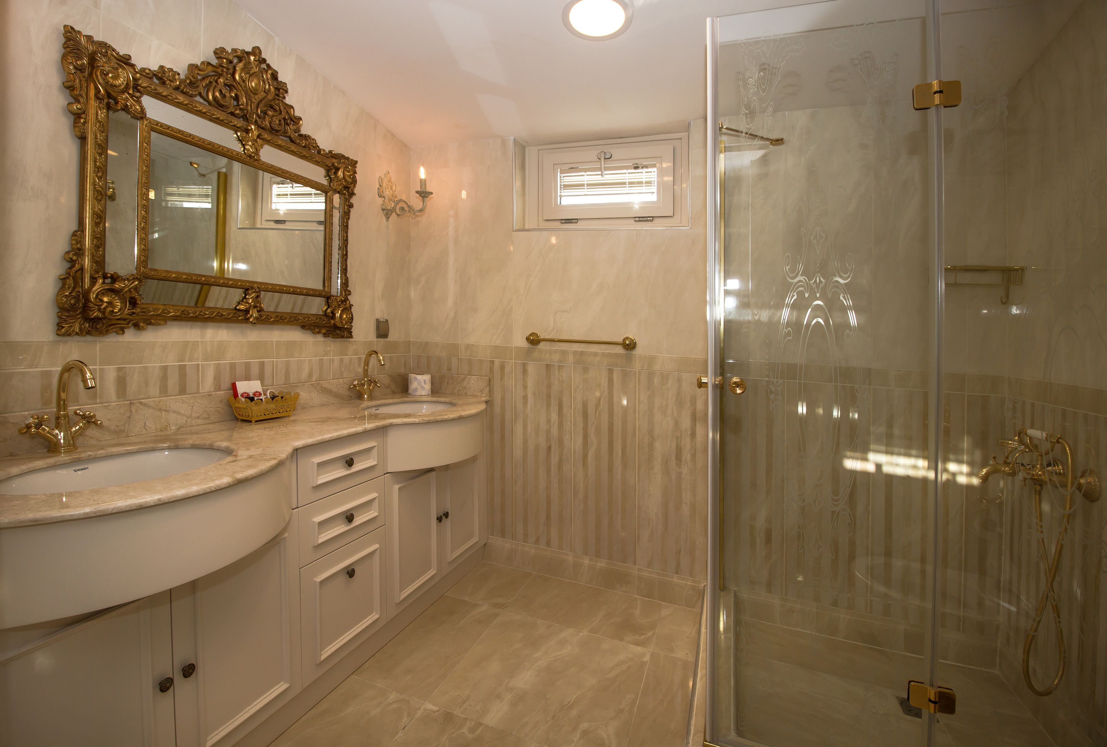 A bathroom with two sinks, a large ornate mirror, a glass shower enclosure, and marble flooring.