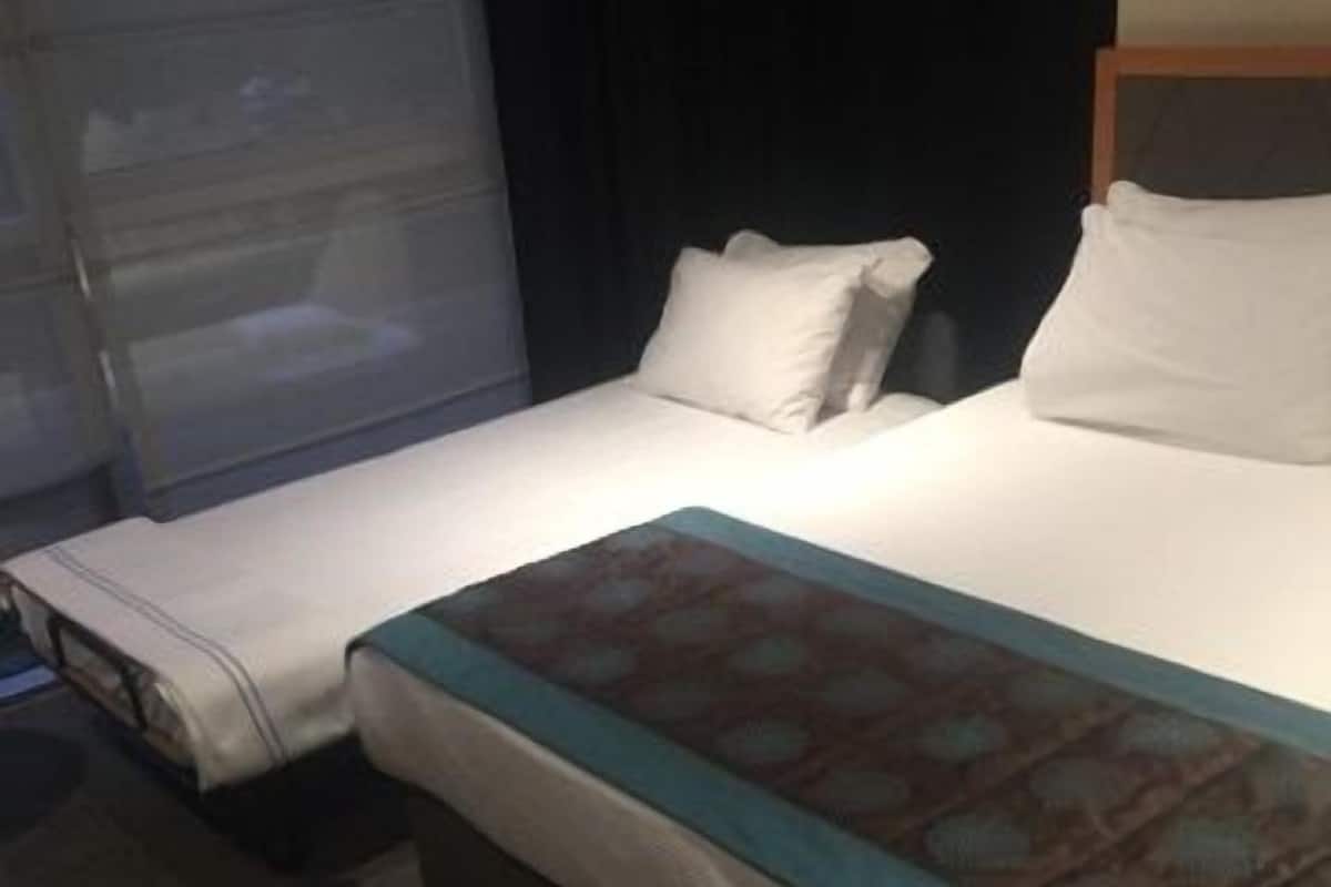 A hotel room with a bed, a bedside table, and a window with curtains.