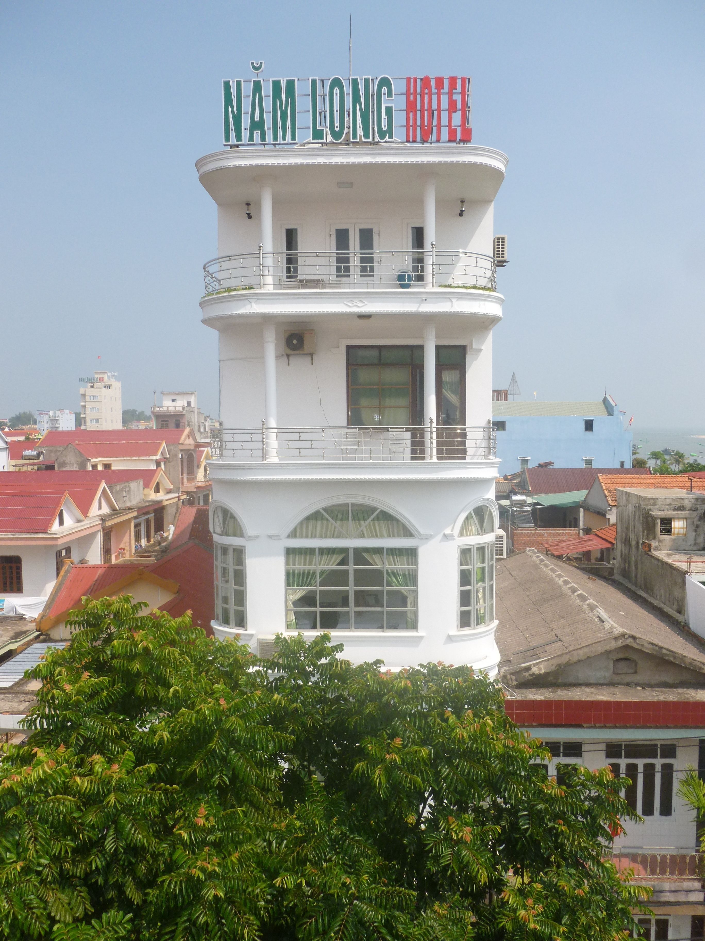 A white tower with "NAM LONG HOTEL" signage. It features multiple windows and balconies.