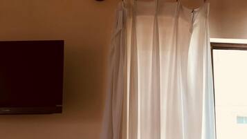 A room with a white curtain, a mounted TV, and an air conditioning unit on the wall.