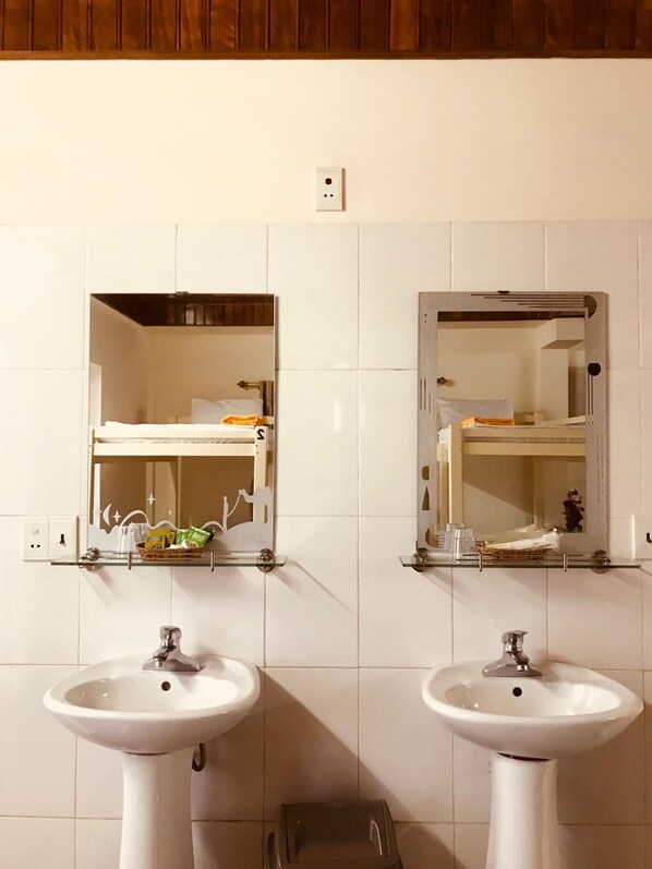 A bathroom with two sinks, a mirror, and a shelf with toiletries.