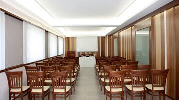 Une salle de conférence avec des rangées de chaises en bois, une table centrale et un design moderne au plafond.