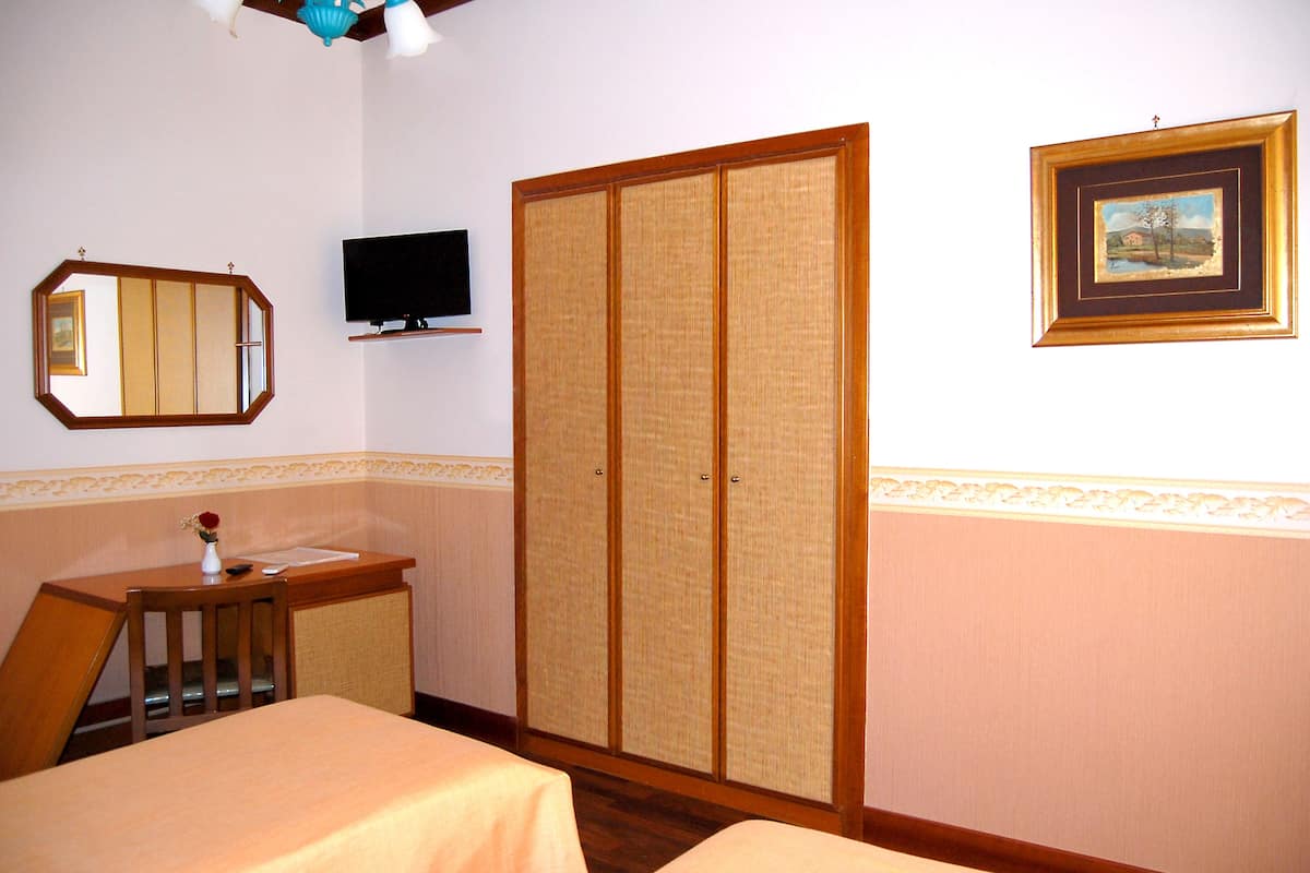 A hotel room with a bed, a desk with a chair, a television, a wardrobe, and a framed picture on the wall.