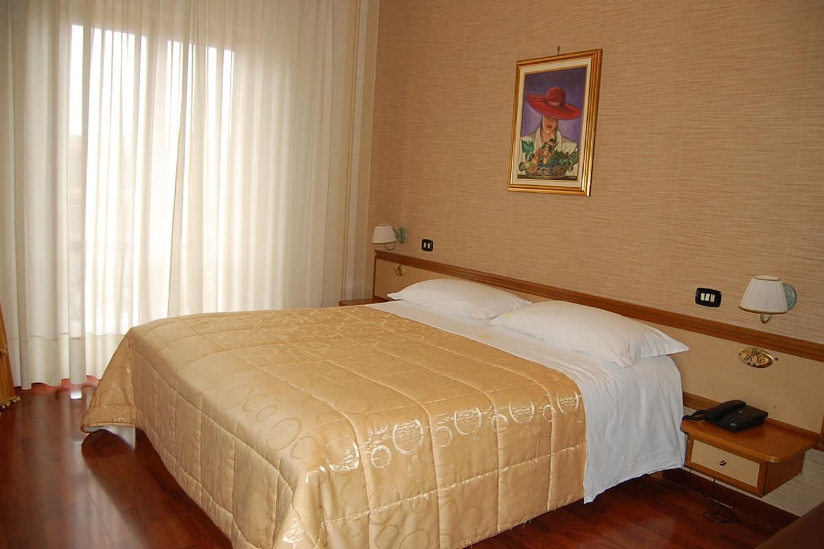 A hotel room with a large bed, a bedside table with a lamp, a phone, and a painting on the wall.