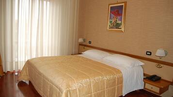 Ein Hotelzimmer mit einem großen Bett, einem Nachttisch mit Lampe, einem Telefon und einem Bild an der Wand.