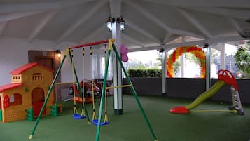 Children can play under the shaded tent with a swing set, playhouse, and slide on the artificial turf floor.