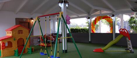 Zona de juegos infantiles con un columpio, una casita y un tobogán.