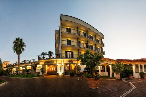 A multi-story hotel with a curved facade, balconies, and a well-lit entrance.