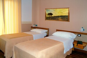 Two single beds with white linens, a painting of a landscape on the wall, and a bedside table with a lamp and a phone.