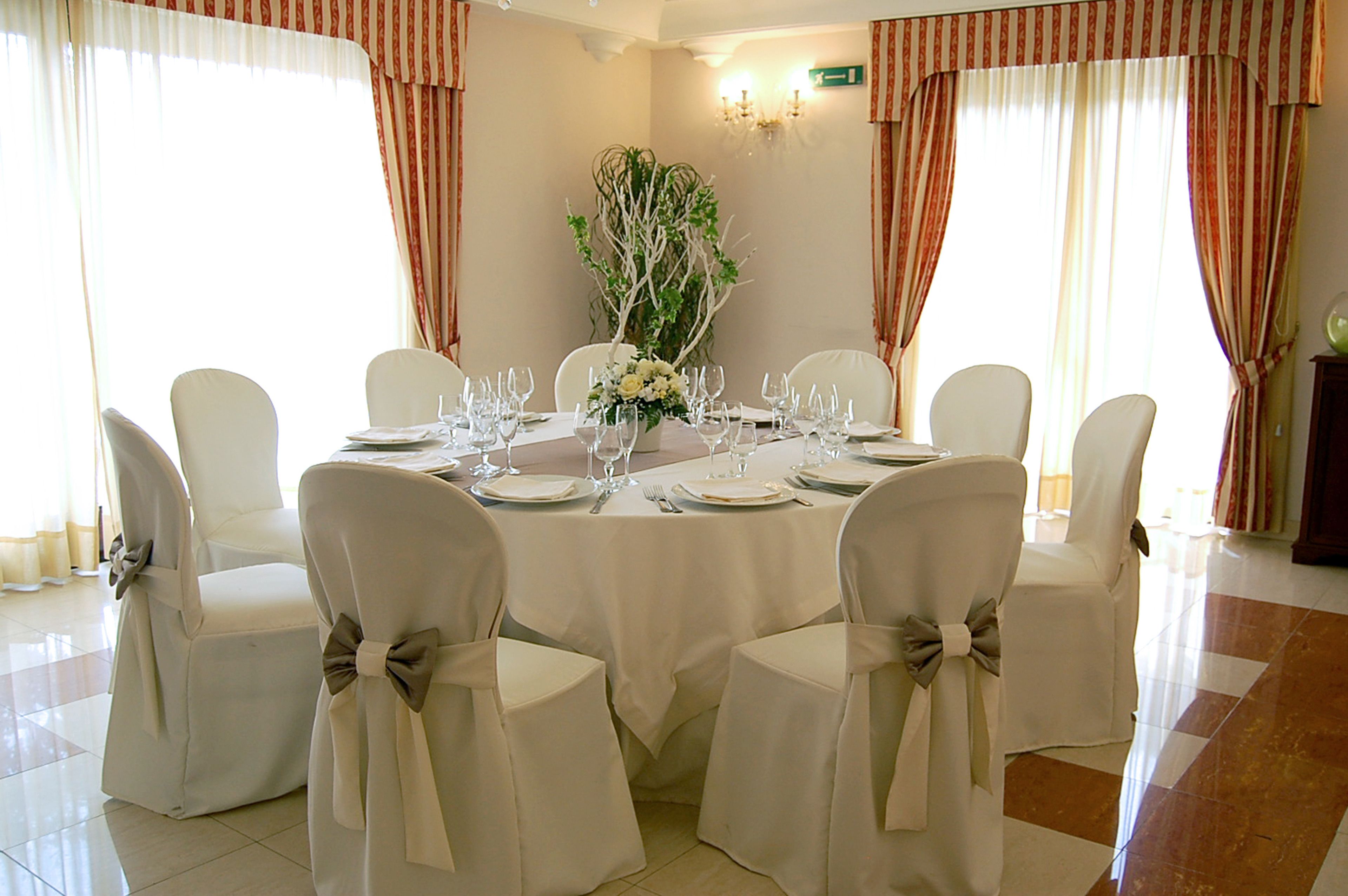 A dining area with a round table set for six, surrounded by six chairs with bow ties.