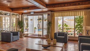 A lobby with wooden ceiling, seating area, potted plants, and a view of the outside. - Aparthotel Calema Avenida Jardim (Vila Real Santo Antonio)