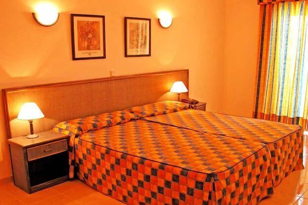A hotel room with a large bed, two bedside lamps, and two framed pictures on the wall.