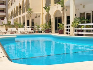 A swimming pool with lounge chairs and potted plants, surrounded by a building with arched windows and balconies. - Aparthotel Calema Avenida Jardim (Vila Real Santo Antonio)