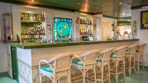 A bar area with wicker chairs, a counter with various bottles, and a colorful painting on the wall. - Aparthotel Calema Avenida Jardim (Vila Real Santo Antonio)