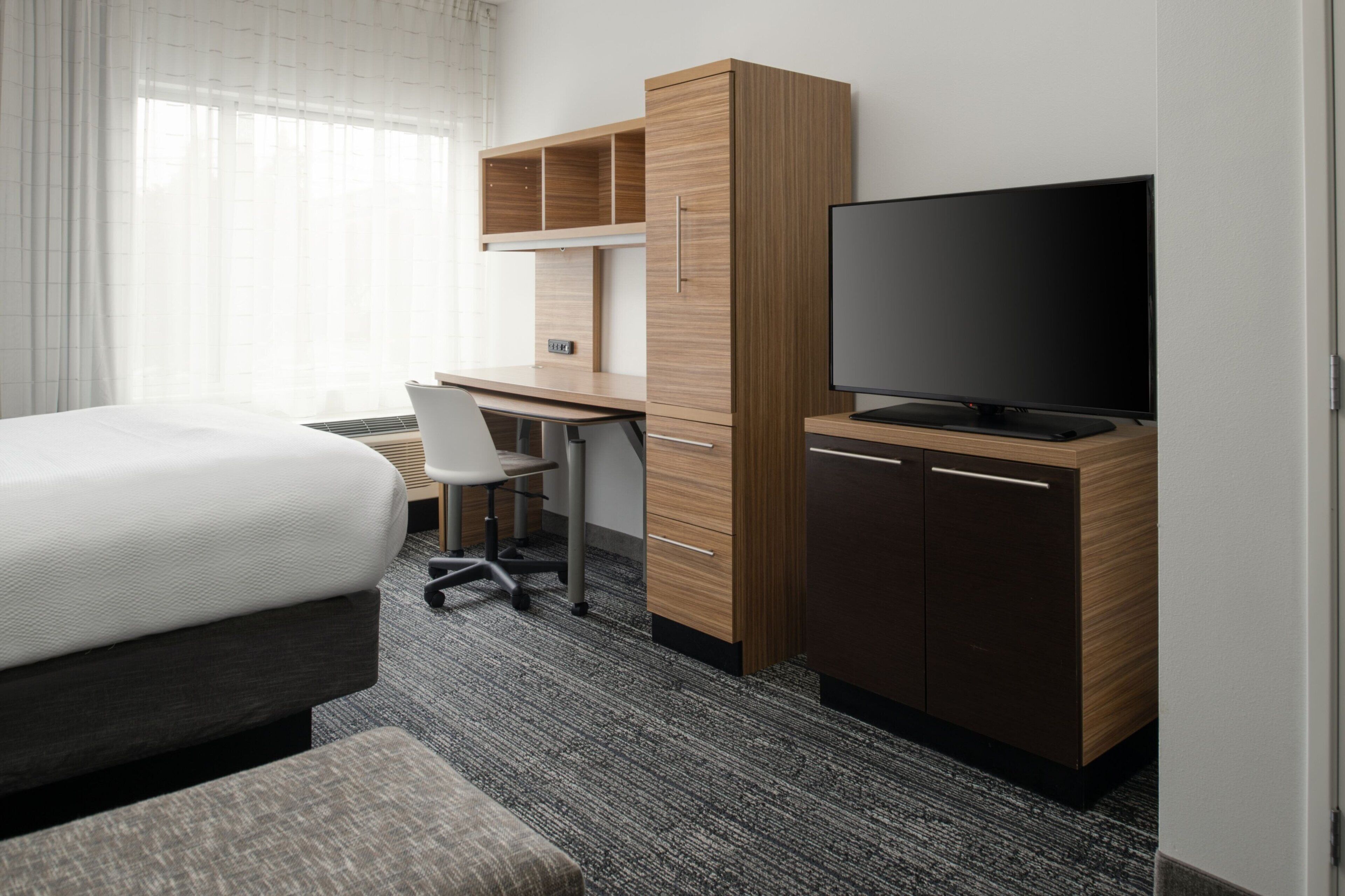 Ett hotellrum med en säng, ett skrivbord med en stol, en tv och en garderob.
