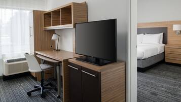 A hotel room with a wooden desk, a television, a bed, and a window with curtains.