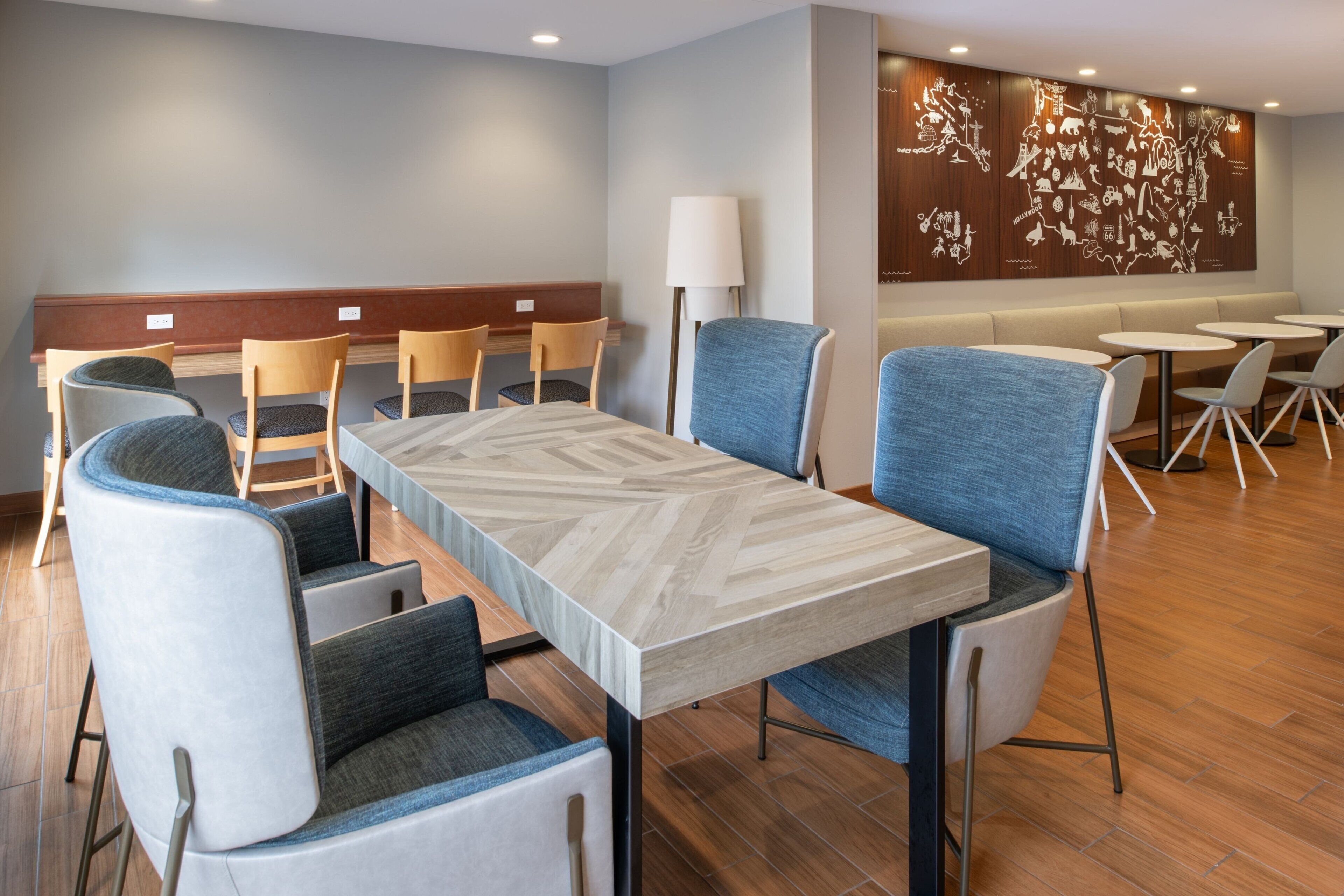 A modern hotel lobby with a long dining table, several chairs, and a wall with a map mural.