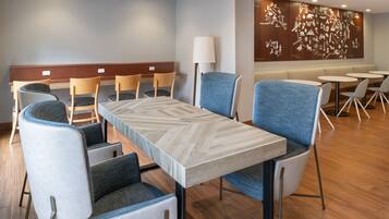 A modern hotel lobby with a long dining table, several chairs, and a wall with a map mural.