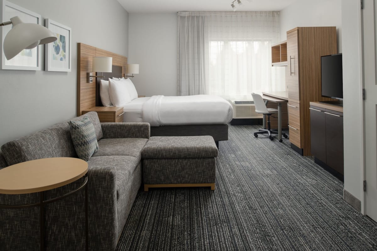 Hotellihuone, jossa on sänky, sohva, työpöytä, televisio ja ikkuna, jossa on verhot.