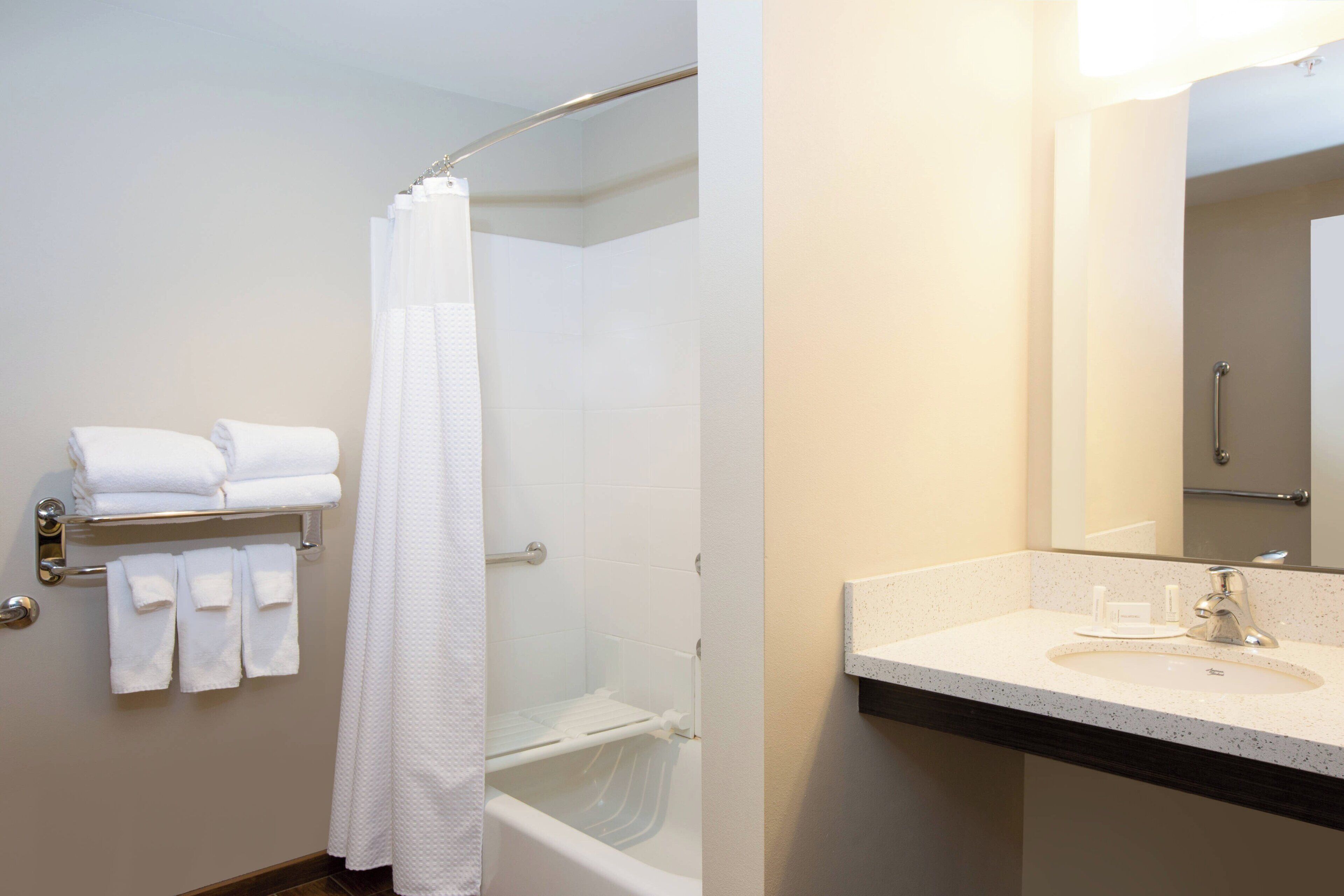 A bathroom with a shower, a sink, and a towel rack with folded towels.