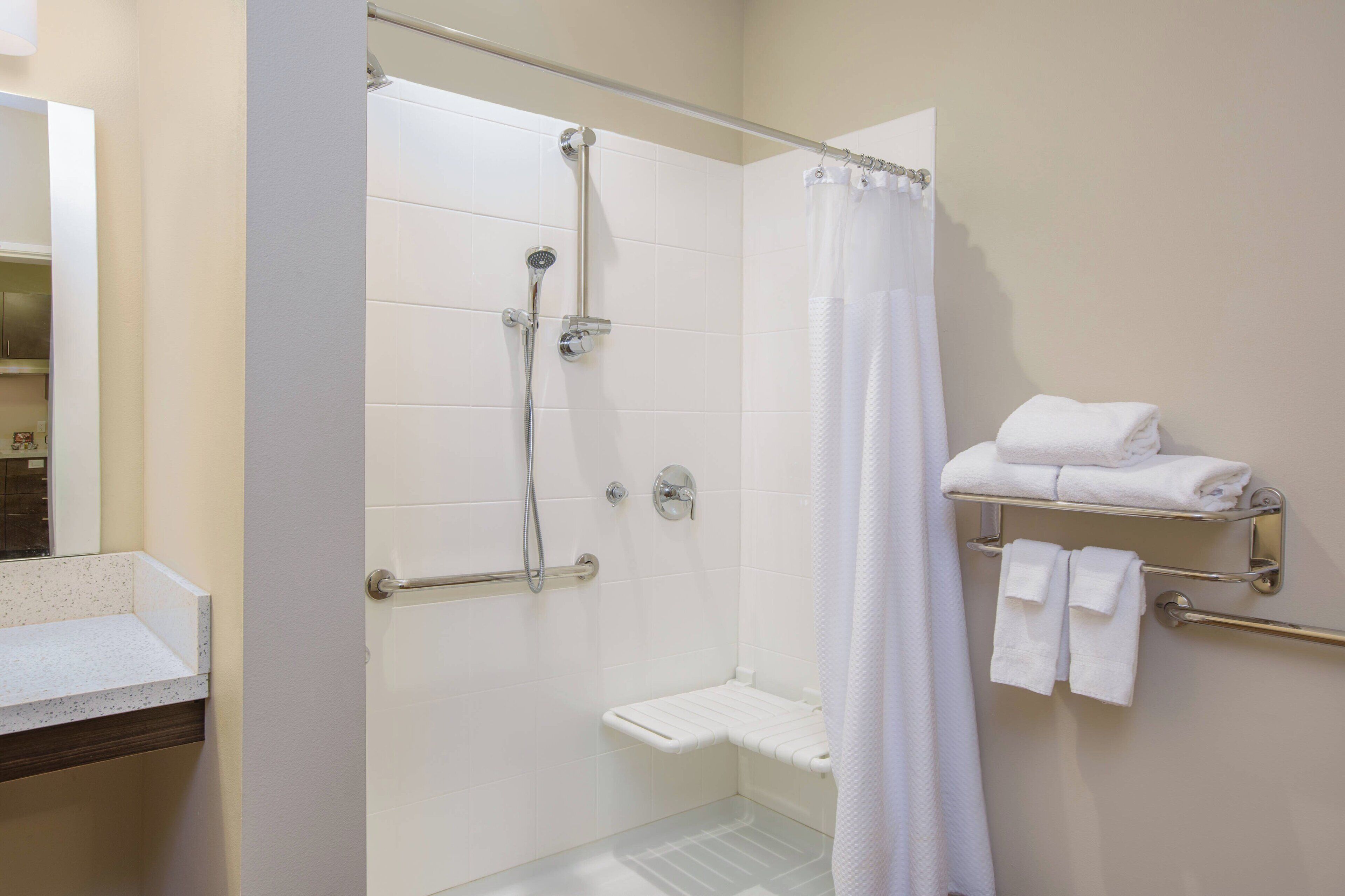 Un baño moderno con cabina de ducha de vidrio, azulejos blancos, un inodoro y un perchero con toallas dobladas.