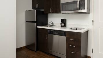 A compact kitchen with stainless steel appliances, a dishwasher, and dark wooden cabinets.