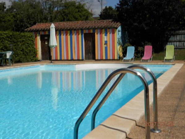 A swimming pool with a metal ladder, a colorful building with vertical stripes, and three lounge chairs. - Le Relais des 5 Chateaux (Vezac)