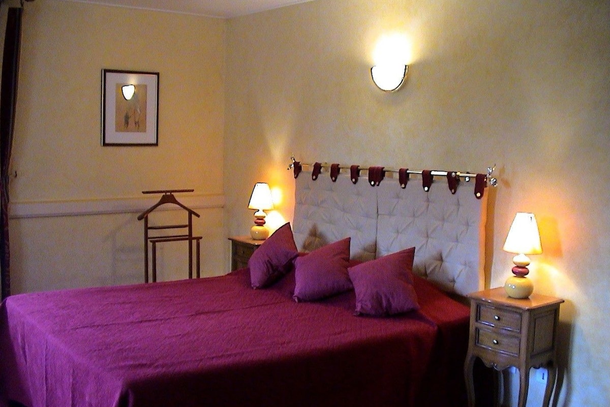 A neatly made bed with a headboard, two bedside tables with lamps, a framed picture on the wall, and a coat rack.