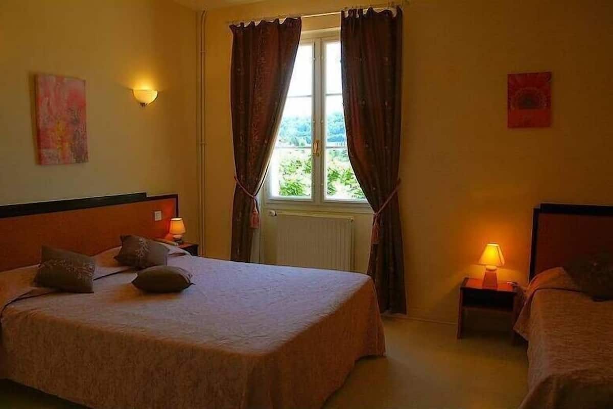 A hotel room with a large bed, two bedside lamps, a window with curtains, and a radiator.