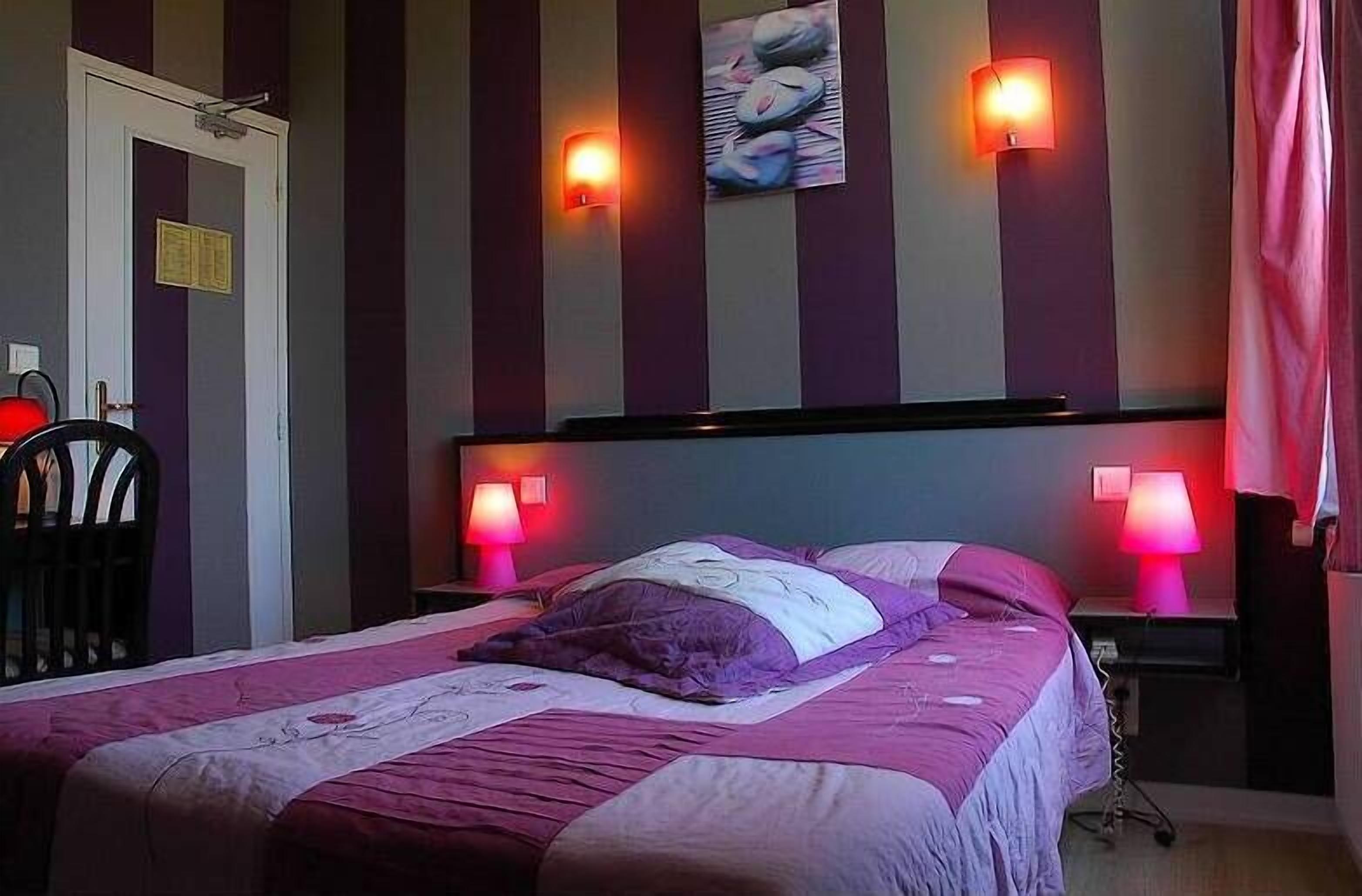 Una habitación de hotel con una cama, dos lámparas de noche, una silla y una puerta.