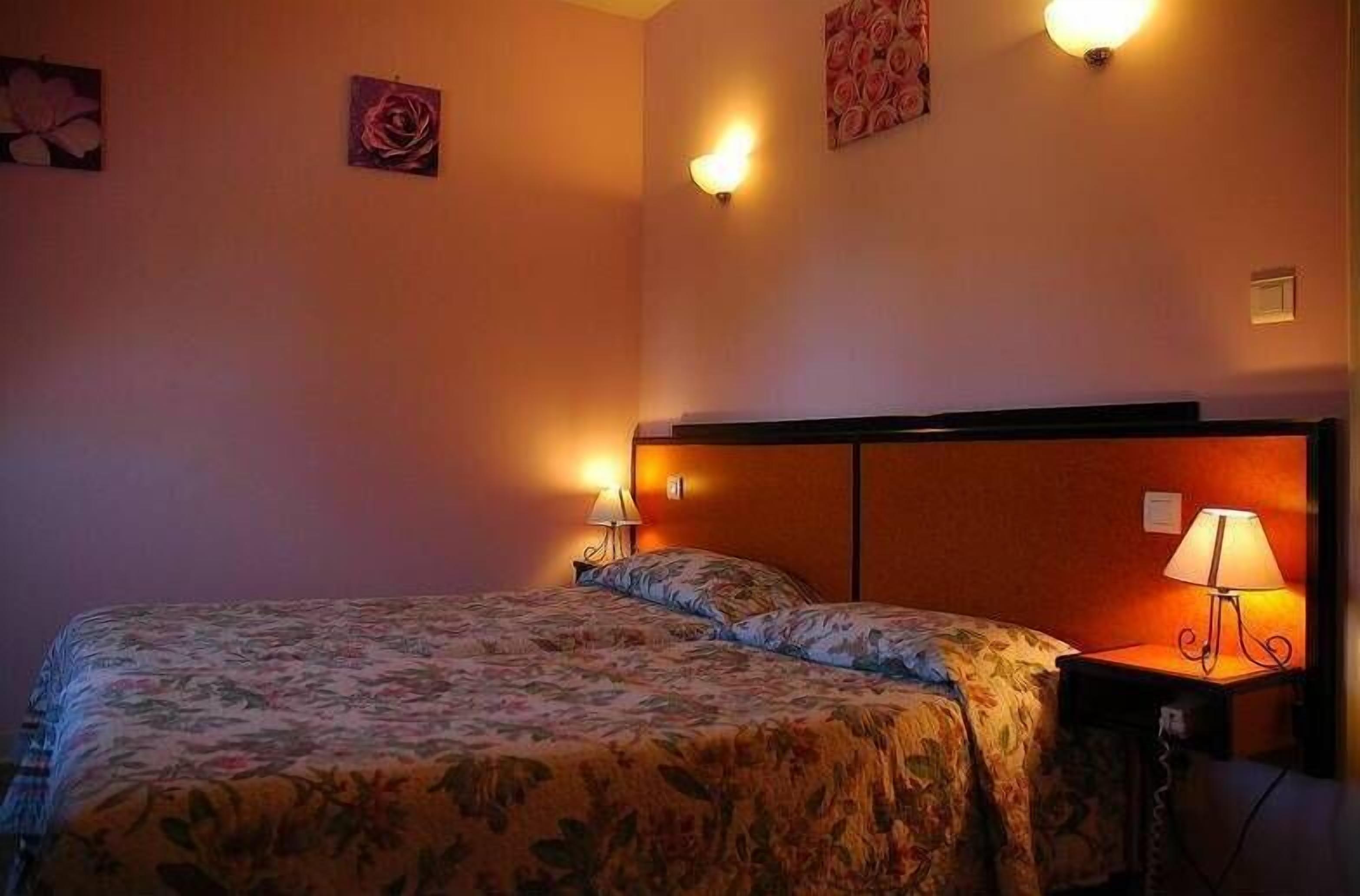 Habitació d'hotel amb un llit, dues làmpades laterals i decoració floral a la paret.