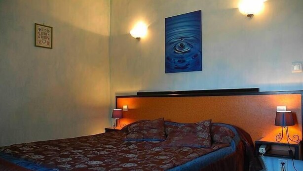 Una habitación de hotel con una cama grande, dos lámparas de noche, una obra de arte colgada en la pared y una mesita con una lámpara.