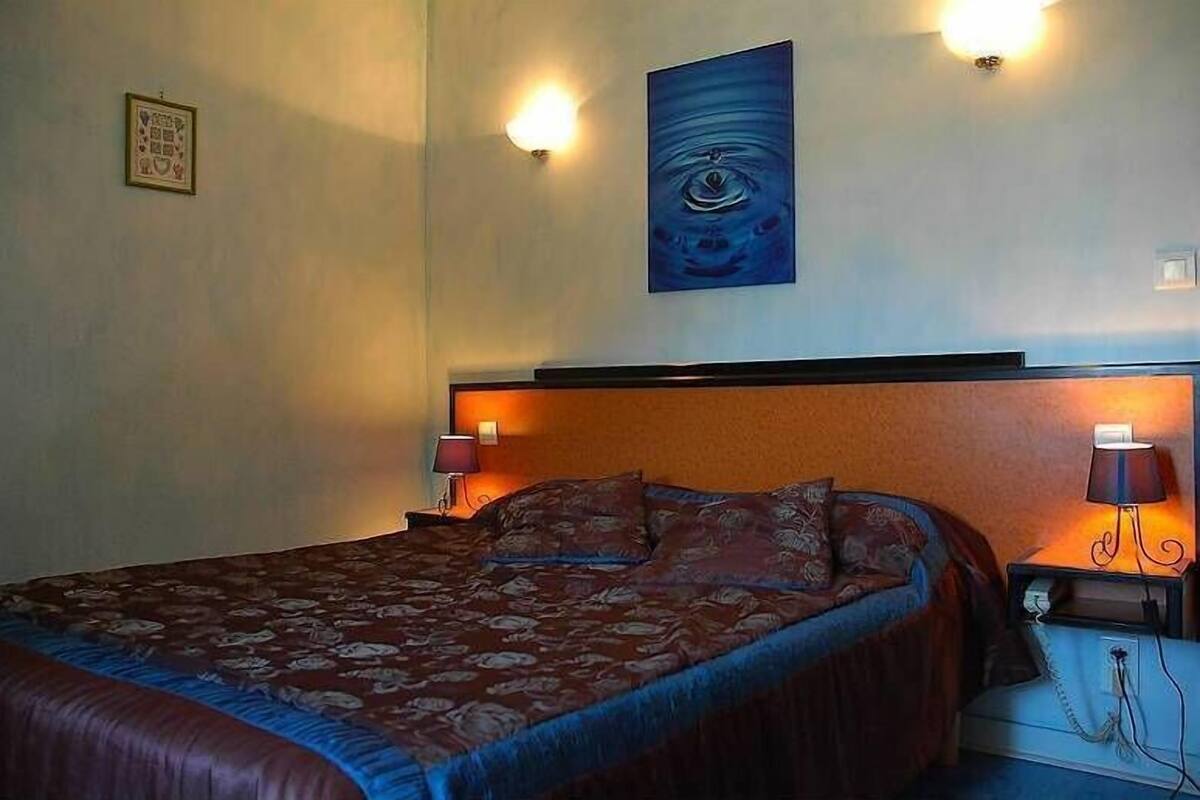 A hotel room with a large bed, two bedside lamps, a wall-mounted artwork, and a small table with a lamp.