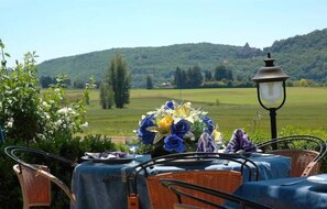An outdoor dining area with wicker chairs and a table set for two, overlooking a scenic landscape with hills and a distant building. - Le Relais des 5 Chateaux (Vezac)