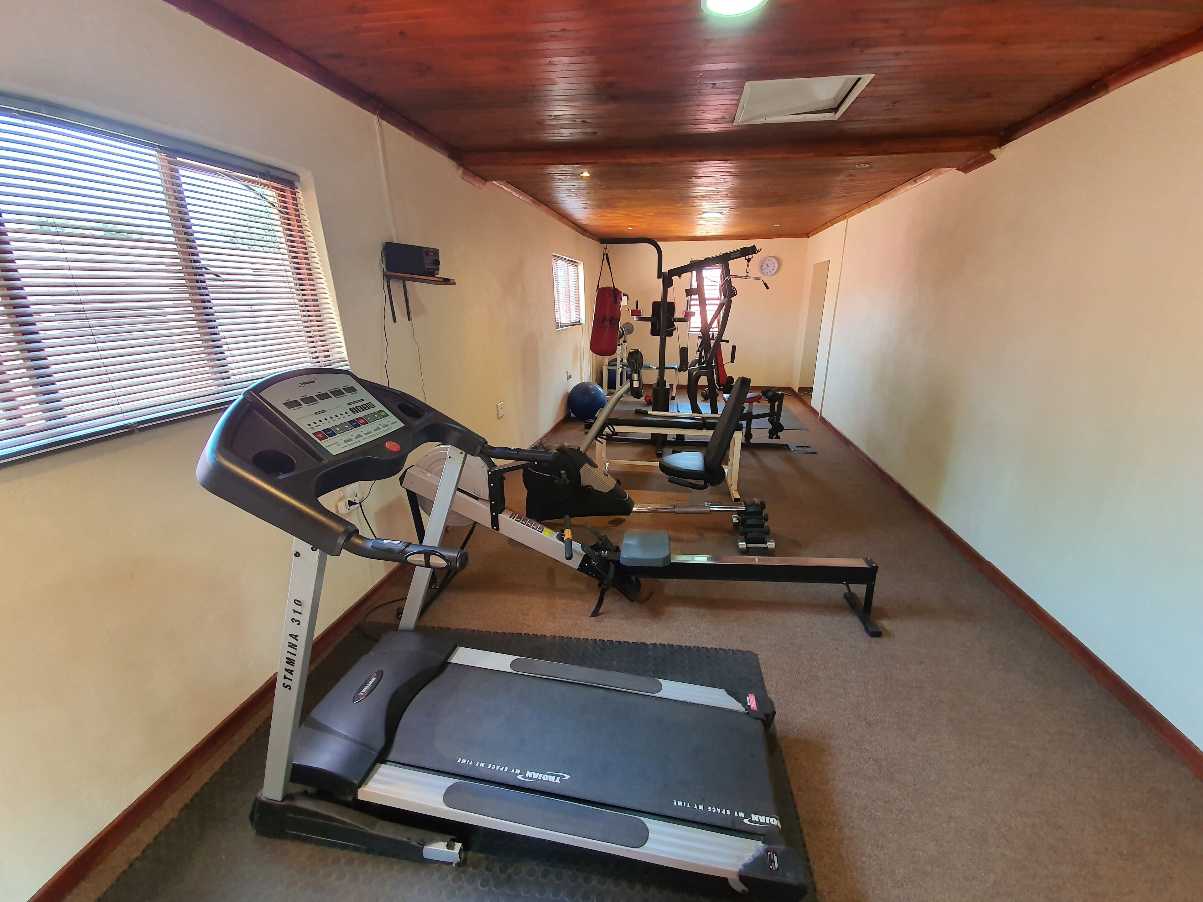 Un gimnasio con cintas de correr, una prensa de pesas y un reloj en la pared.